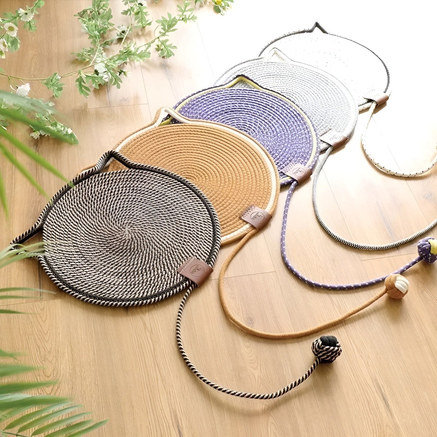 Geflochtene Katzenbettmatten in Schwarz, Beige, Lila und Grau auf Holzboden, mit Spielzeug.