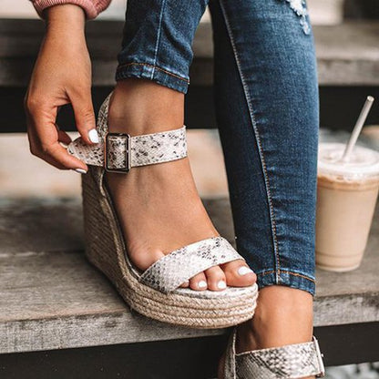 Frau trägt Schlangenleder-Plateausandalen, Jeans; modische Sommermode, Damen-Schuhe.