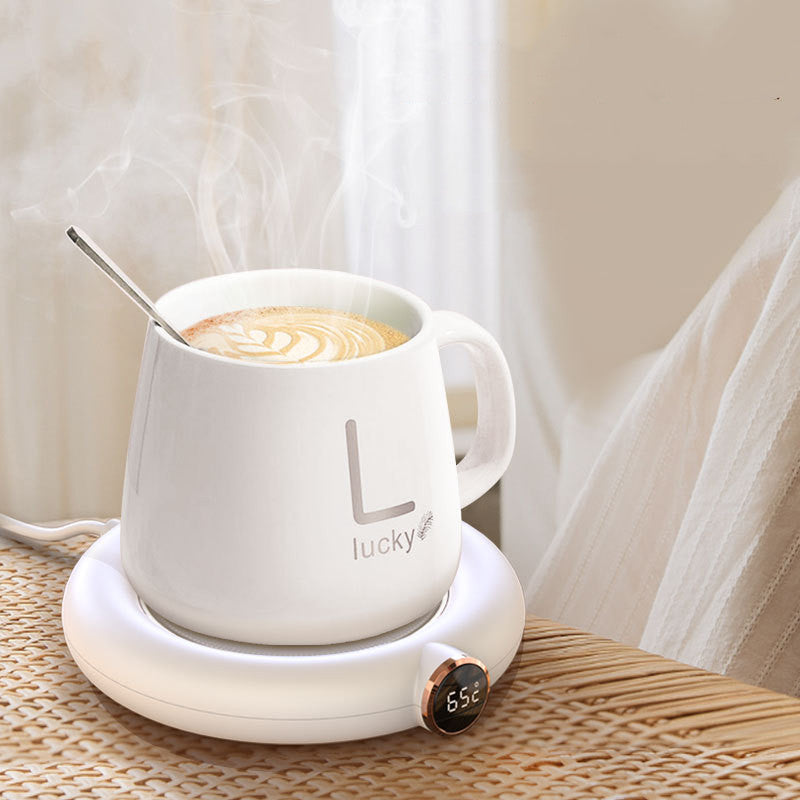 Weiße Tasse mit Löffel auf elektrischem Tassenwärmer, Kaffee mit Latte Art, Tisch, Dampf.