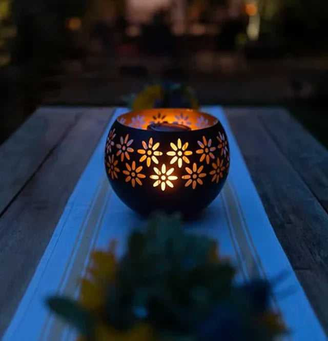 Schwarze Metall-Laterne mit Blumenmuster, beleuchtet, auf Holztisch im Freien.