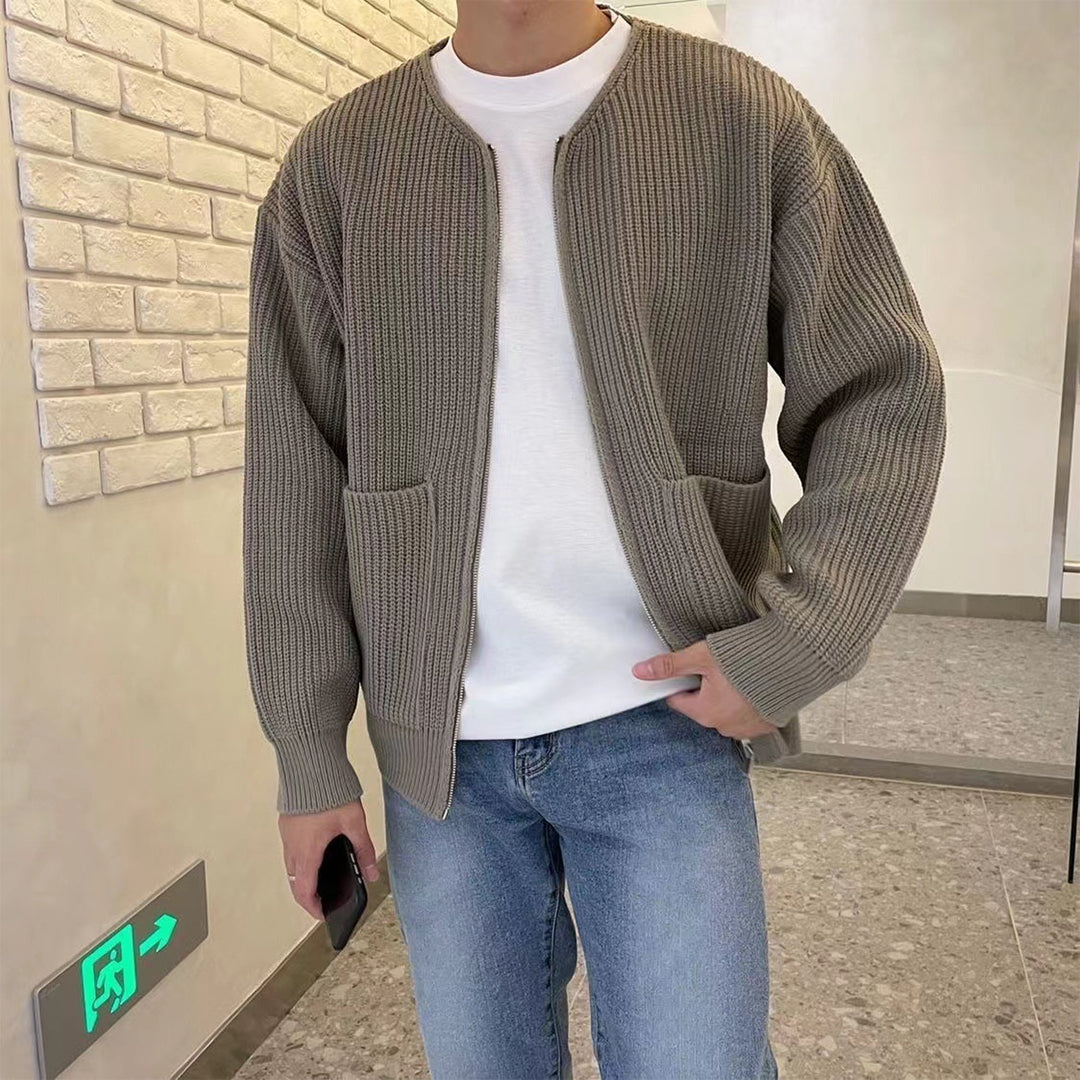 Mann in khakifarbener Strickjacke, weißem Shirt und blauer Jeans in modernem Raum.