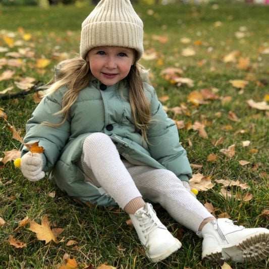 Mädchen in grüner Kinderparka, beige Mütze, Herbstlaub, Outdoor-Kleidung, warm, bequem.