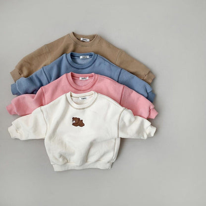 Vier Kinderpullover in Beige, Blau, Rosa und Weiß mit Bärenmotiv auf grauem Hintergrund.
