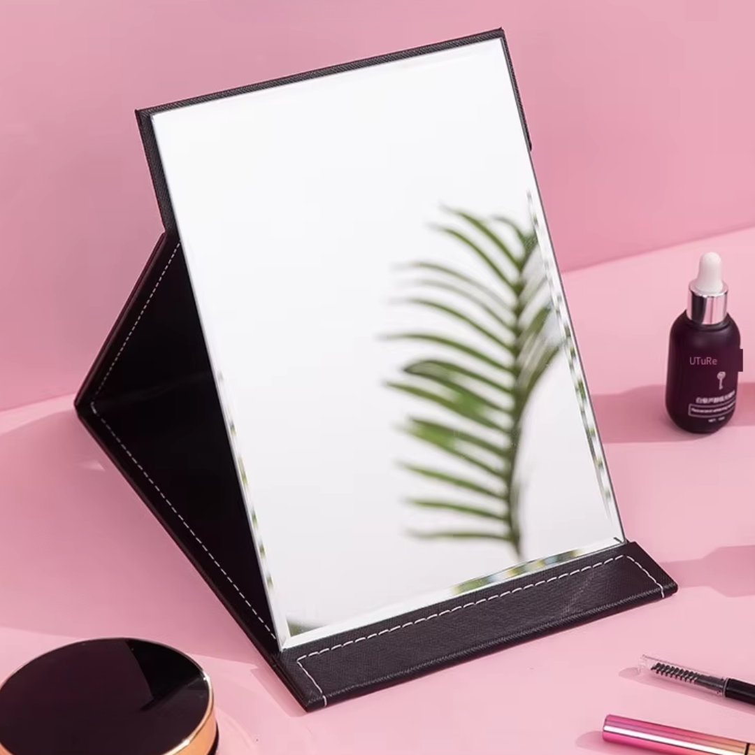 Tragbarer Kosmetikspiegel mit schwarzem Lederrahmen auf rosa Hintergrund, ideal für Make-up.