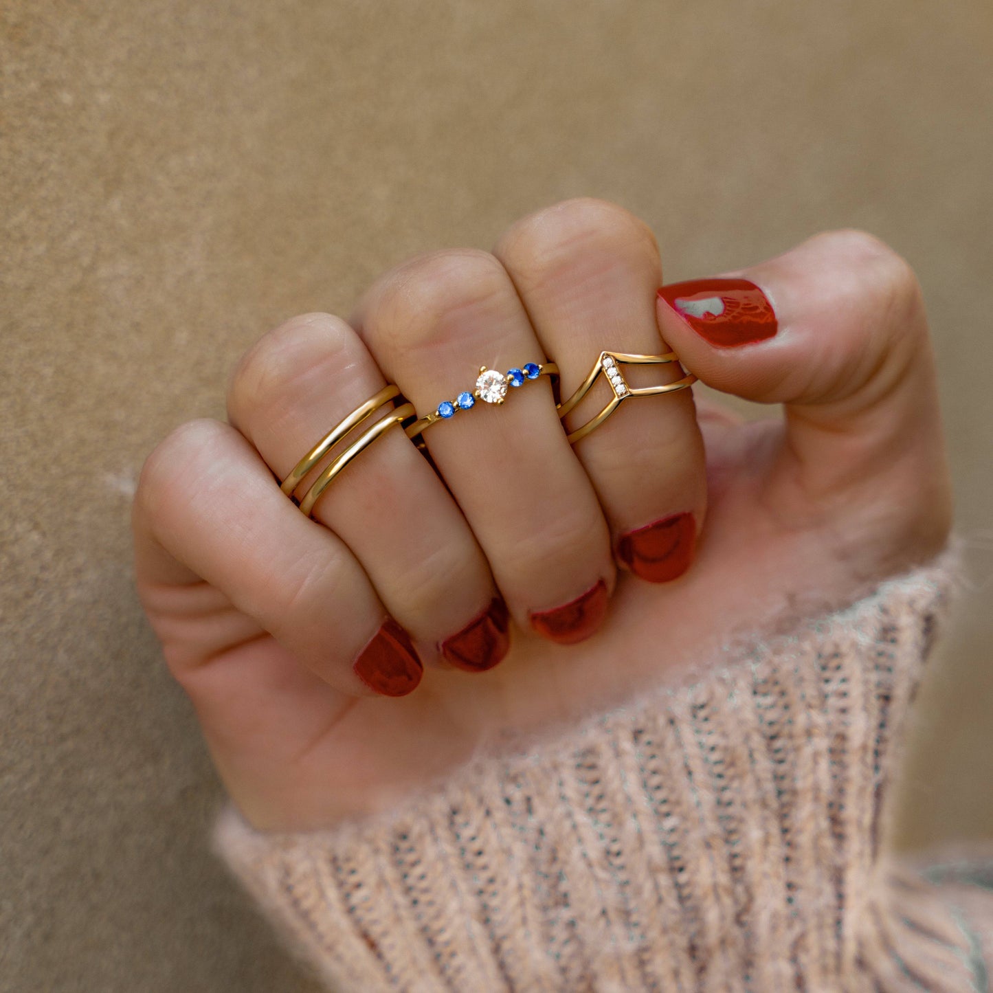 Drei goldene Ringe an Hand, einer mit blauen Steinen und Diamant, modischer Schmuck.