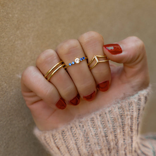 Drei goldene Ringe an Hand, einer mit blauen Steinen und Diamant, modischer Schmuck.