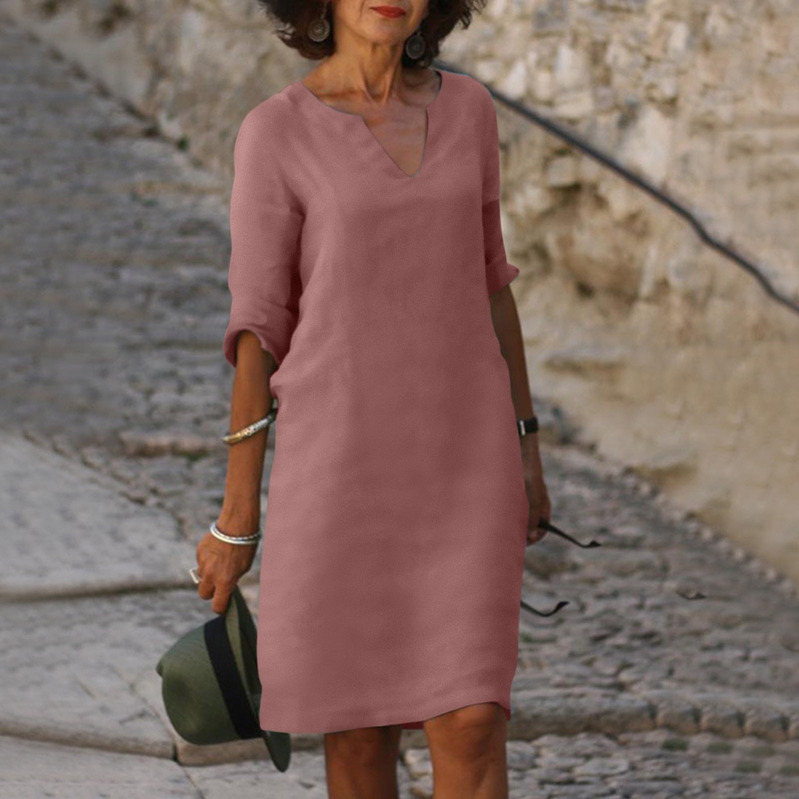 Frau in rosa Leinenkleid, V-Ausschnitt, knielang, auf Kopfsteinpflasterweg.