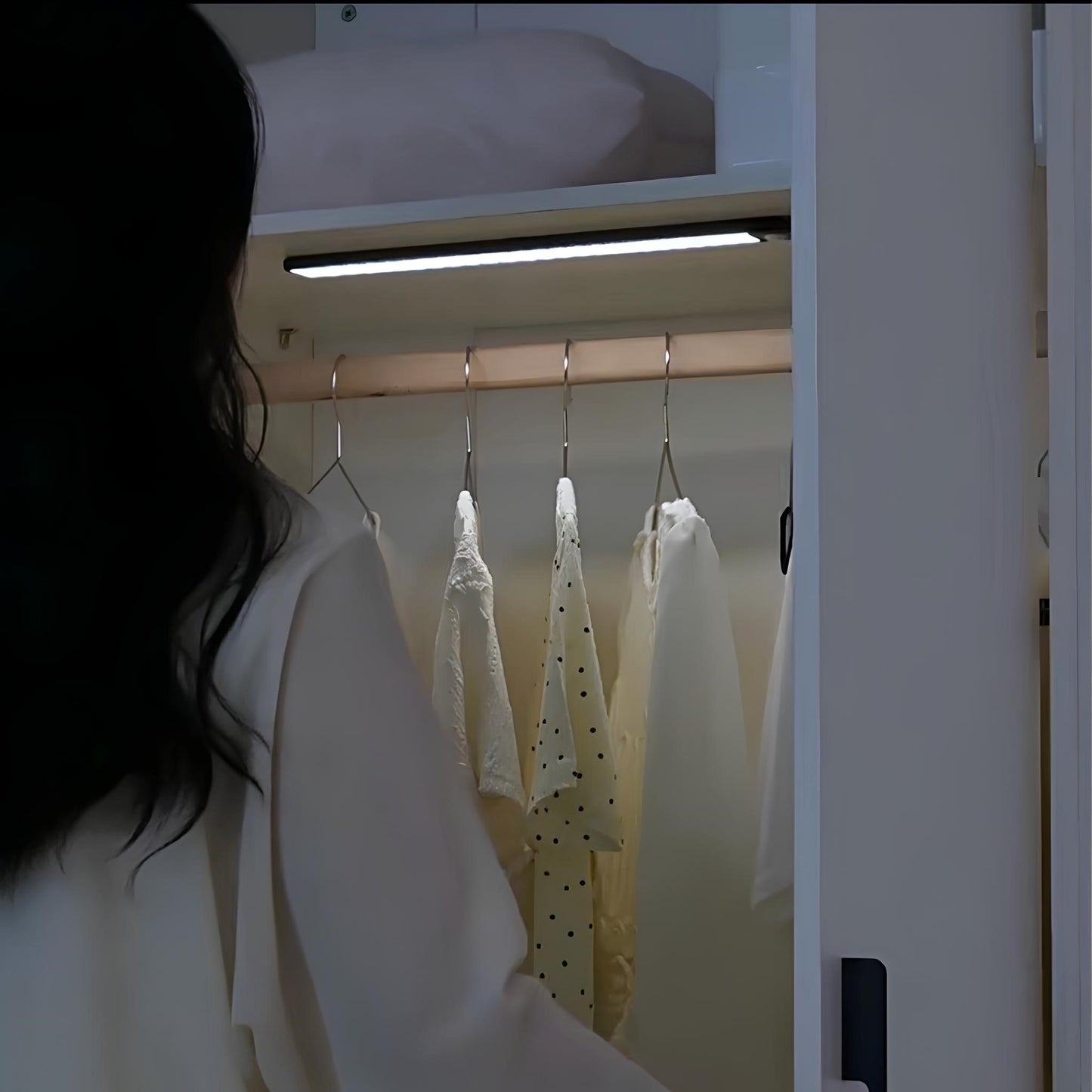 Frau öffnet Kleiderschrank mit beleuchteter Kleiderstange, weiße Blusen, modernes Design.