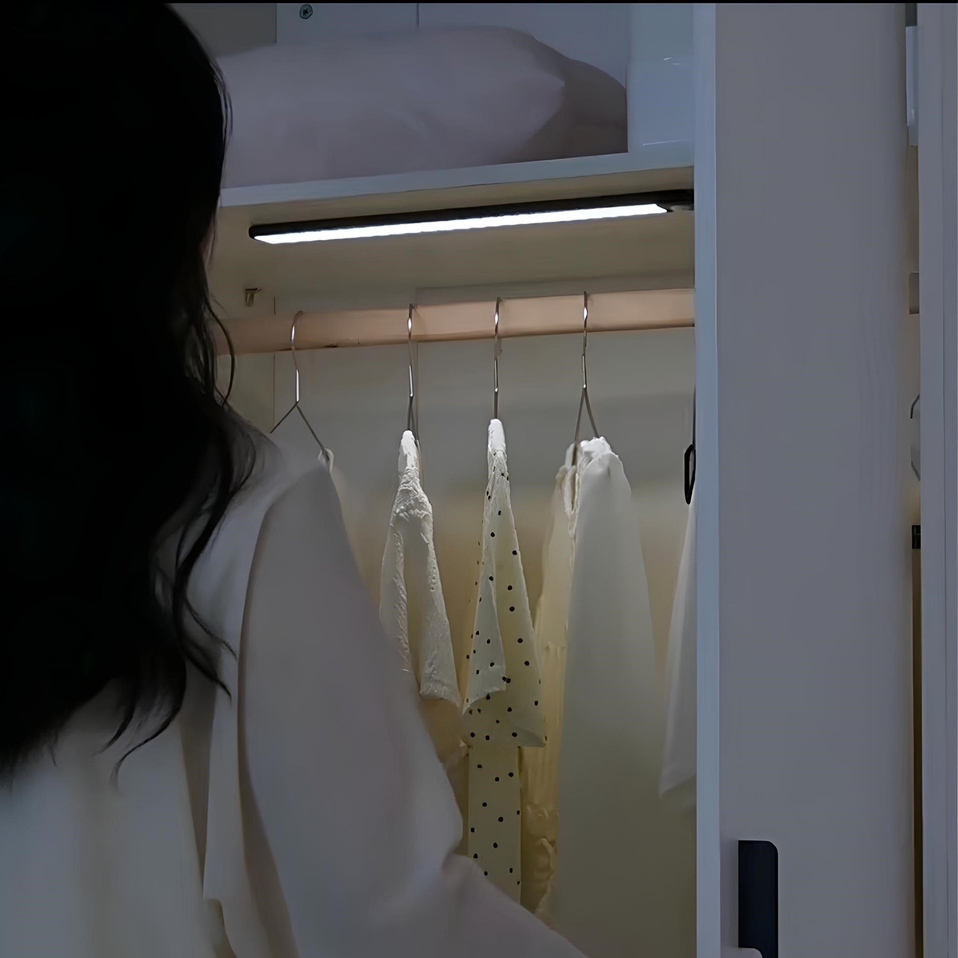 Frau öffnet Kleiderschrank mit beleuchteter Kleiderstange, weiße Blusen, modernes Design.