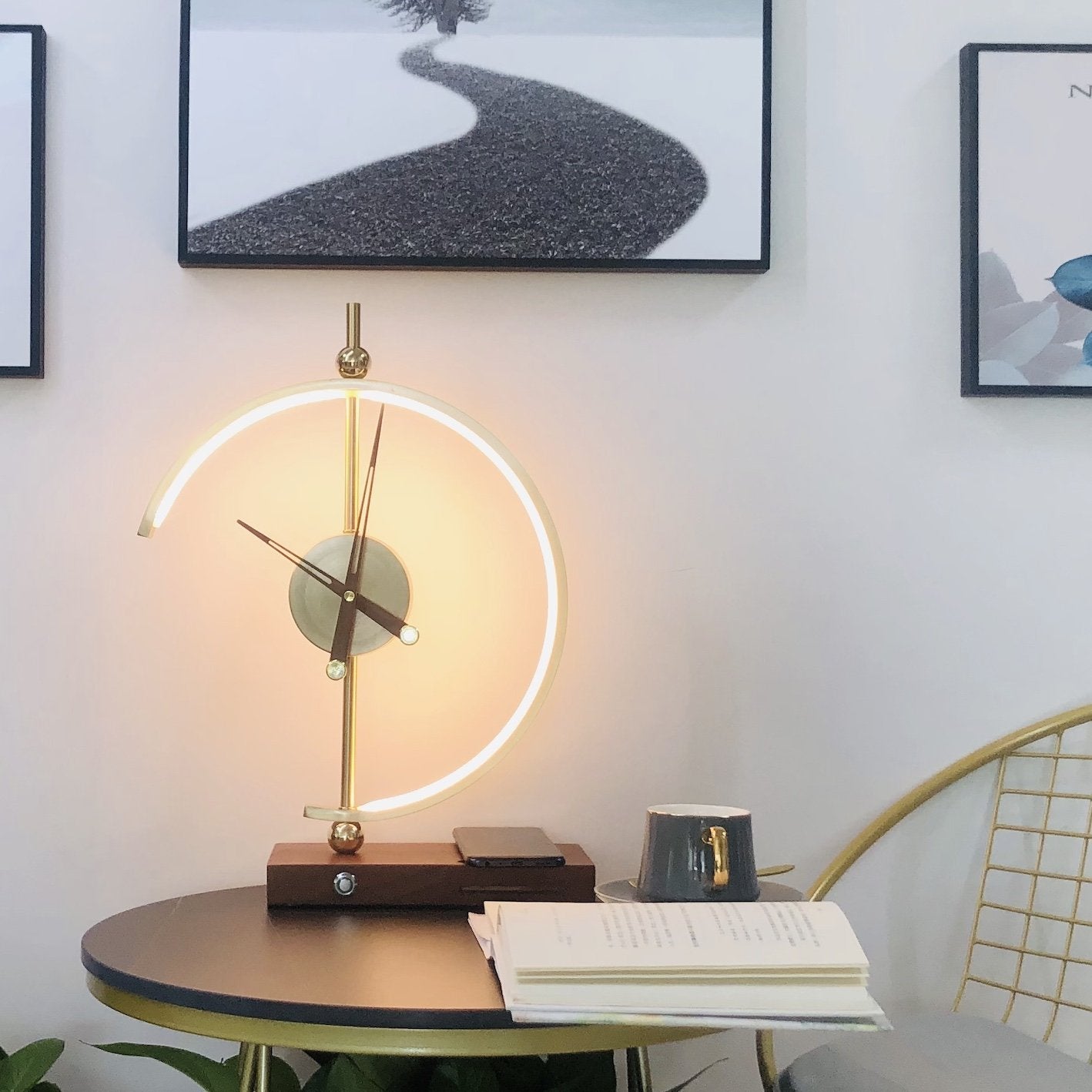 Moderne Tischlampe mit LED-Licht, goldfarben, auf rundem Tisch vor Wandbildern.