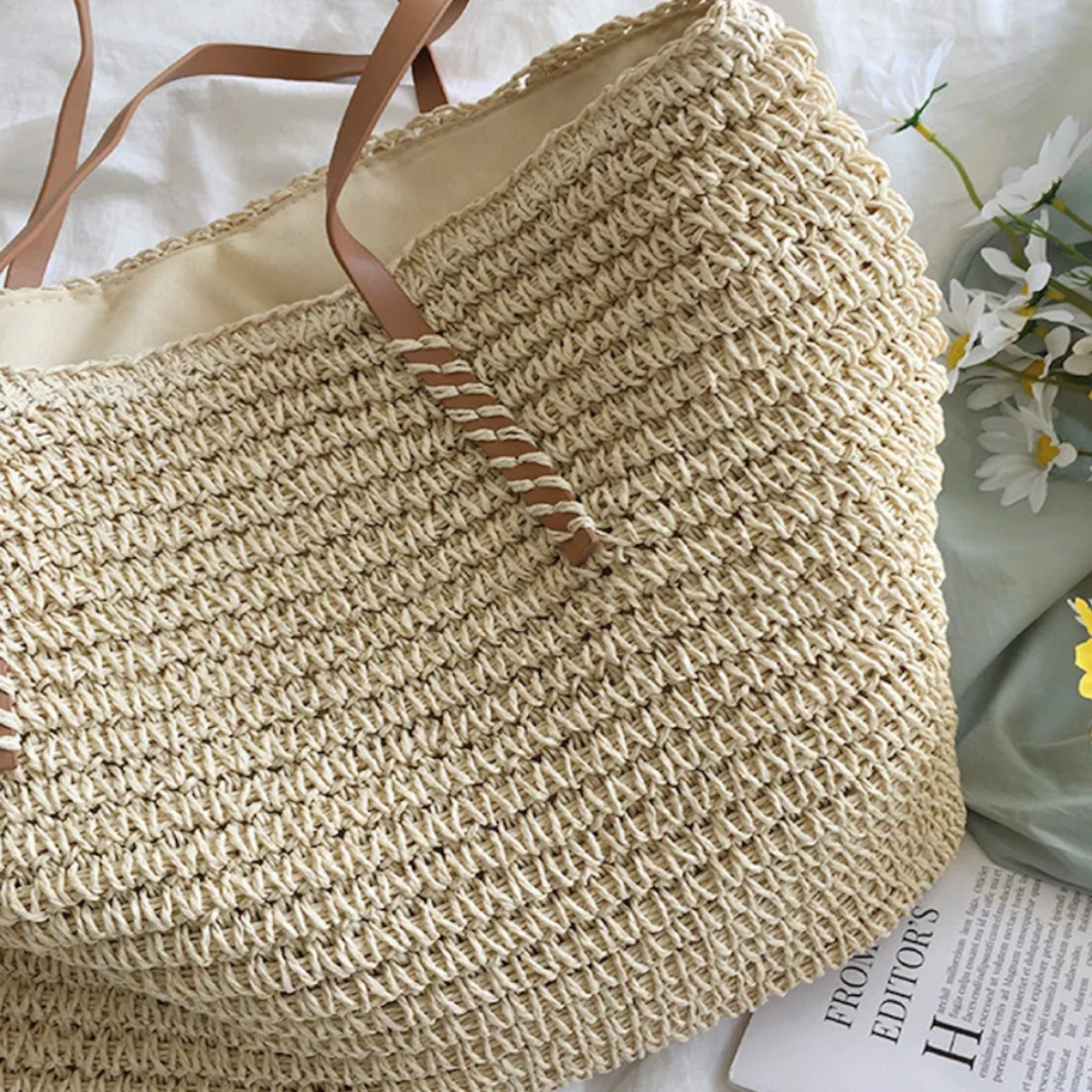 Geflochtene Strohtasche mit braunen Griffen, ideal für Sommer und Strand, auf weißem Hintergrund.