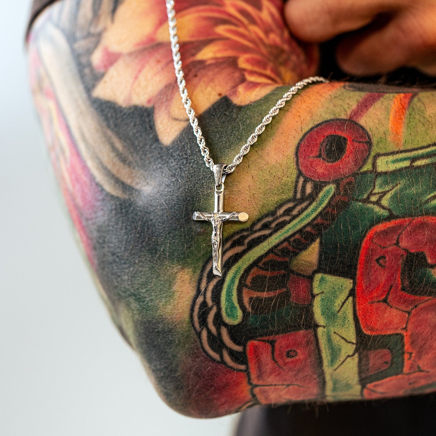 Silberne Kreuzkette auf tätowiertem Arm, Schmuck, Herrenaccessoire, modisch, Edelstahl.