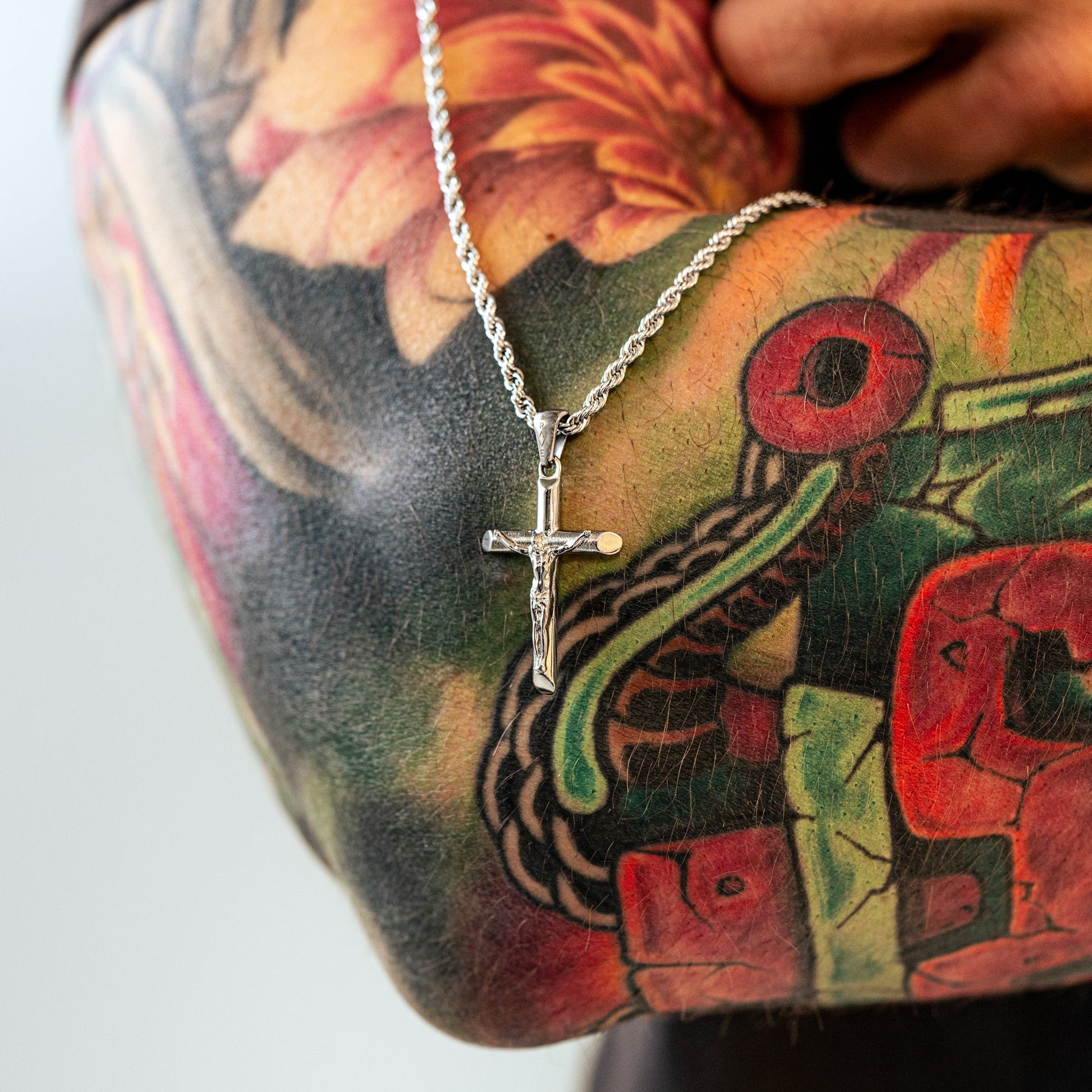 Silberne Kreuzkette auf tätowiertem Arm, Schmuck, Herrenaccessoire, modisch, Edelstahl.
