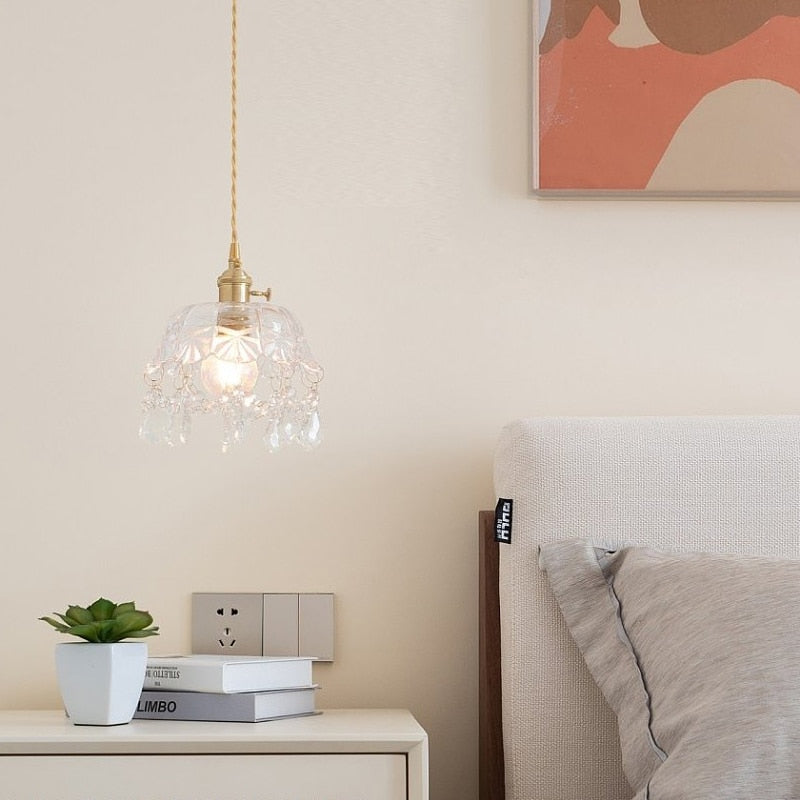 Hängelampe aus Glas mit Kristallen über Nachttisch, modernes Schlafzimmerdekor, beige Wand.