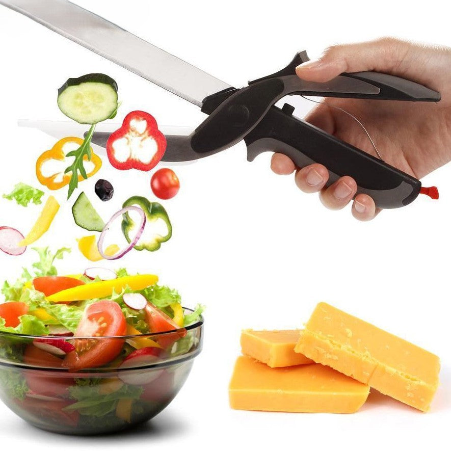Hand hält Küchenschere mit schwarzem Griff, schneidet Gemüse über Salatschüssel, Käsestücke daneben.