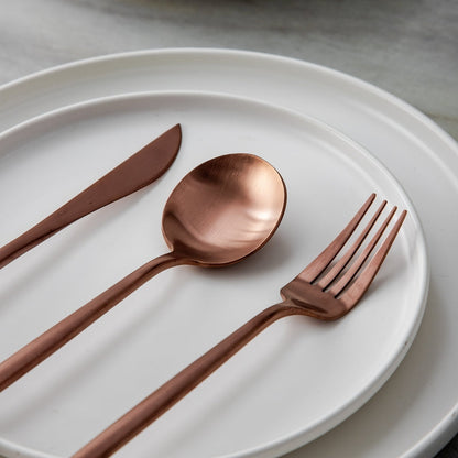 Kupferbesteck-Set auf weißem Teller, bestehend aus Messer, Gabel und Löffel, elegant und modern.