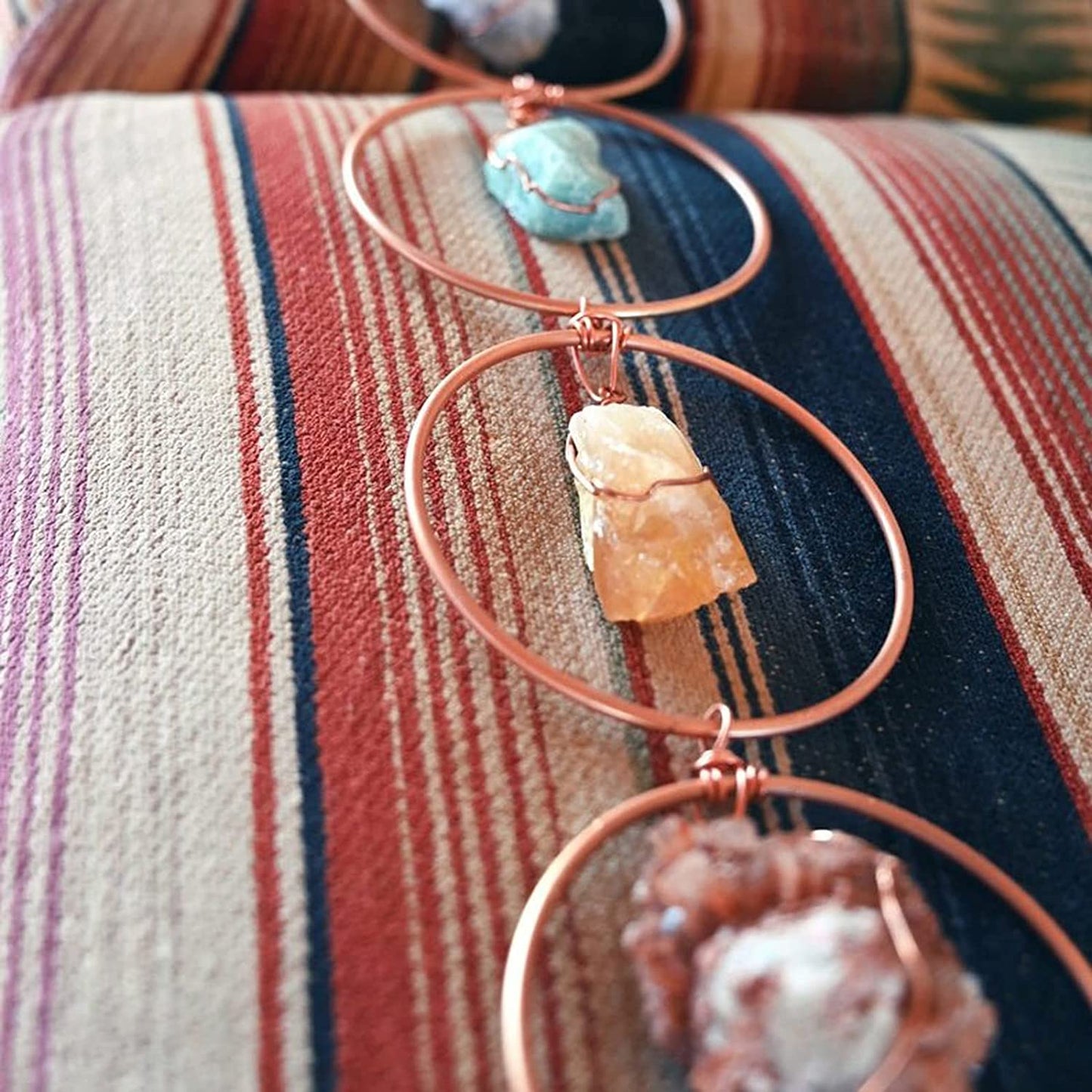 Kupfer-Wanddekoration mit Edelsteinen, handgefertigt, Boho-Stil, auf gestreiftem Stoff.