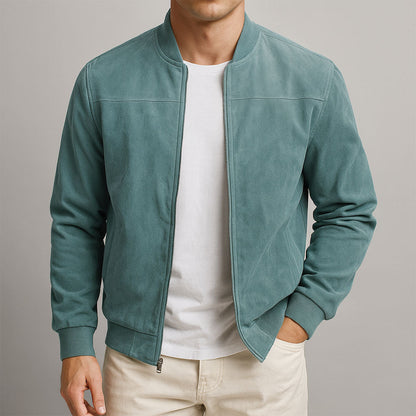 Man bär en grönblå mockajacka med ribbad krage och muddar, öppen dragkedja och vit t-shirt under, ena handen i fickan. 2