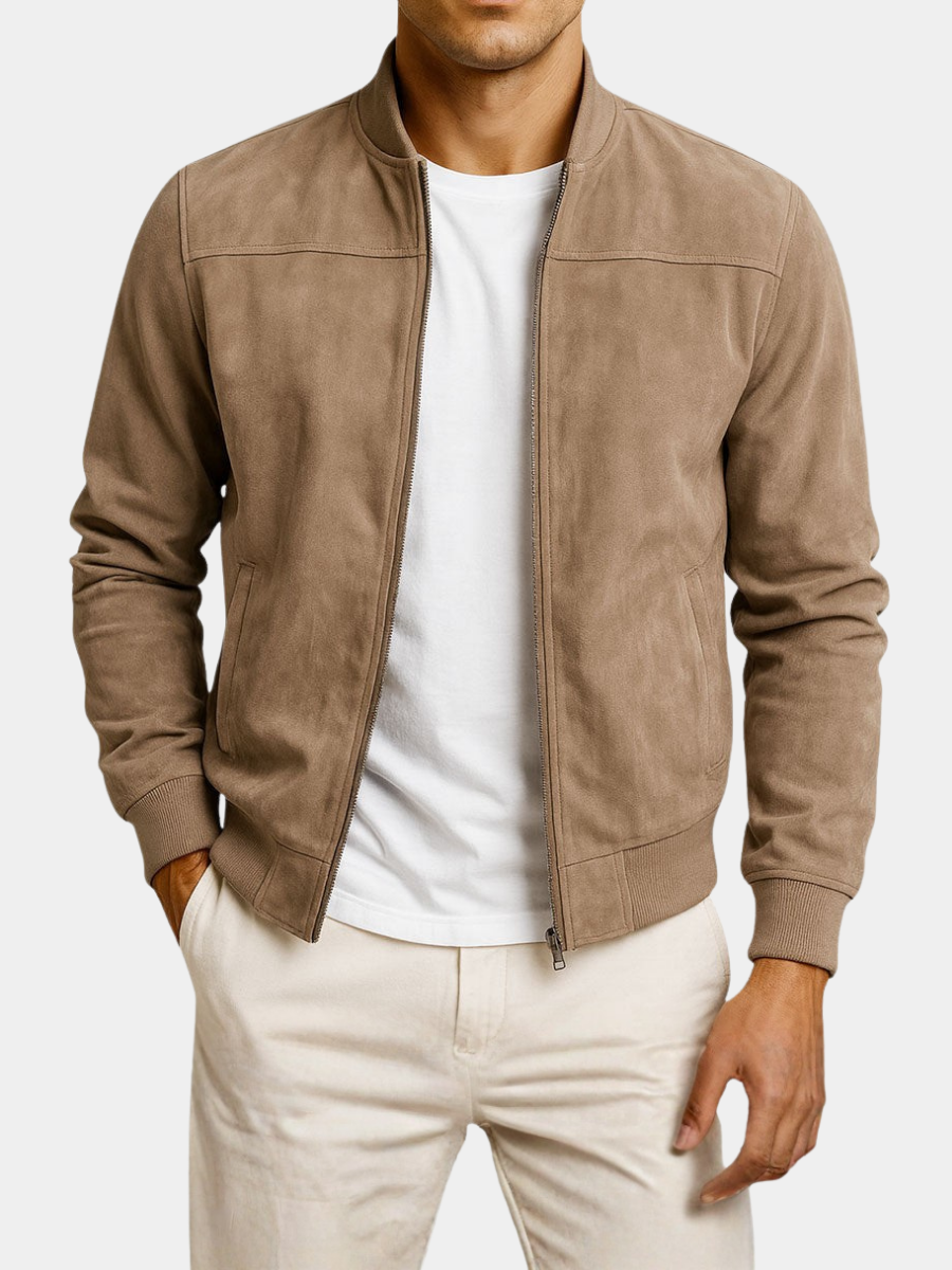 Man i beige mockajacka med öppen dragkedja, vit t-shirt och ljusa byxor, mot ljus bakgrund, med ena handen i fickan. 6