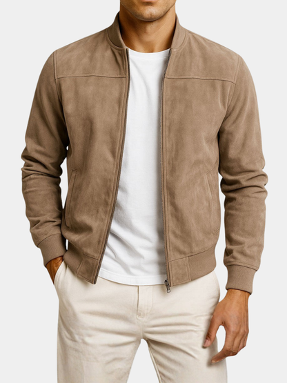 Man i beige mockajacka med öppen dragkedja, vit t-shirt och ljusa byxor, mot ljus bakgrund, med ena handen i fickan. 6