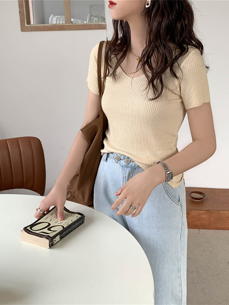 Frau in beigem Rippstrick-T-Shirt, hellblauer Jeans, brauner Tasche, hält Buch.