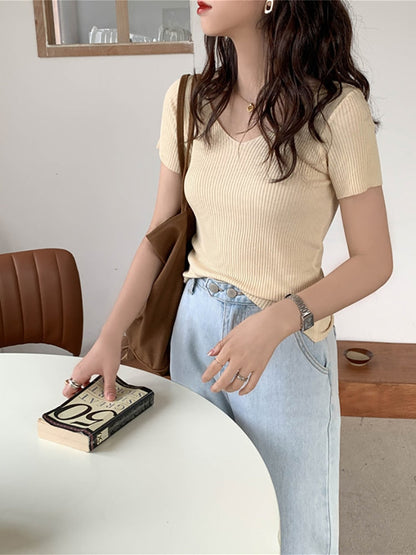 Frau in beigem Rippstrick-T-Shirt, hellblauer Jeans, brauner Tasche, hält Buch.