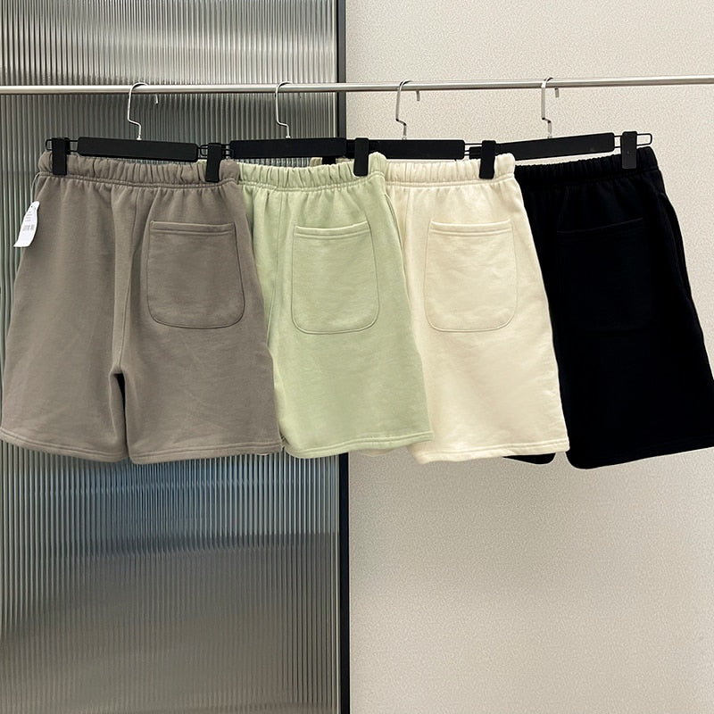 Vier Herren-Shorts in Grau, Grün, Weiß und Schwarz aus Baumwolle auf Kleiderbügeln.