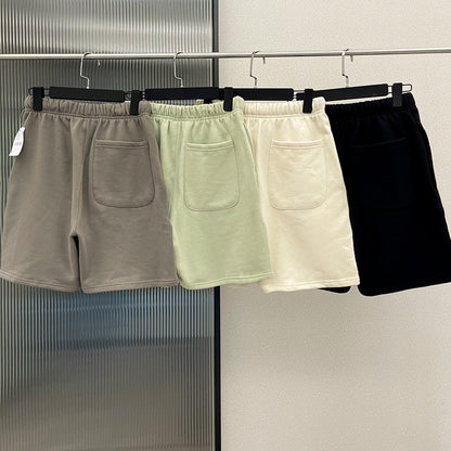 Vier Herren-Shorts in Grau, Grün, Weiß und Schwarz aus Baumwolle auf Kleiderbügeln.