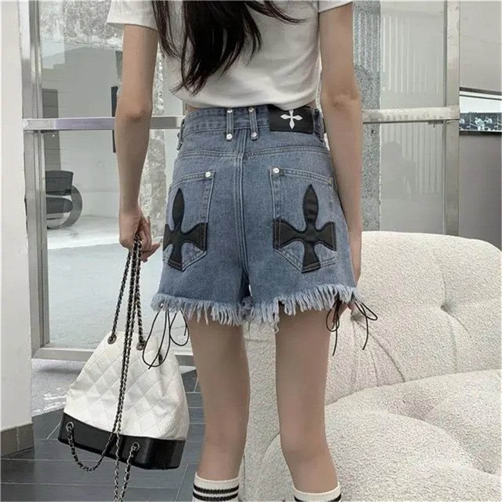 Frau in blauen Jeansshorts mit Kreuzmuster, weißem T-Shirt, hält weiße Handtasche.