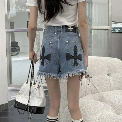 Frau in blauen Jeansshorts mit Kreuzmuster, weißem T-Shirt, hält weiße Handtasche.