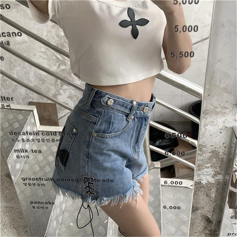 Frau in weißem Crop-Top und blauen Jeans-Shorts mit Fransen vor Spiegel.