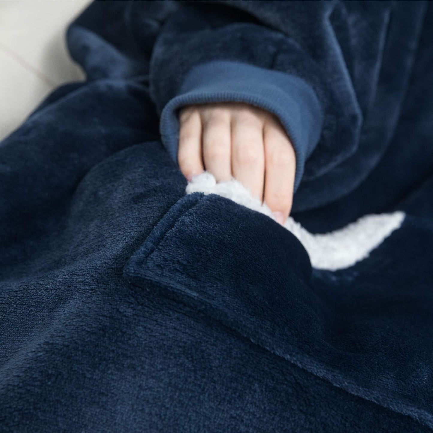 Hand in blauer Fleece-Decke mit Tasche, weiches Material, gemütlich, warm, ideal für kalte Tage.