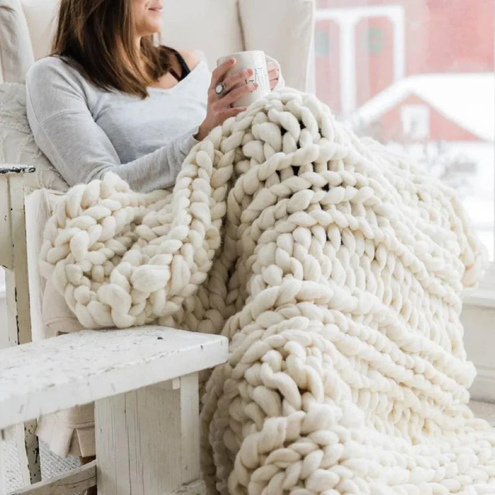Frau mit weißer, grob gestrickter Decke, gemütlich auf Sofa, Winter, Tasse Kaffee, Wohnzimmer.