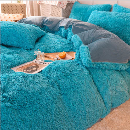 Blaue flauschige Bettdecke aus Kunstfell auf Bett mit Tablett, Zeitschrift und Kerze.