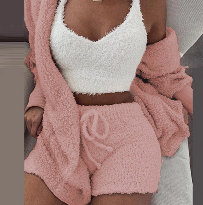 Frau in rosa Fleece-Loungewear-Set, bestehend aus Shorts, Top und Cardigan, auf Sofa.