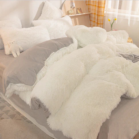 Gemütliches Schlafzimmer mit weißem Kunstfell-Bettwäsche-Set, grauem Kissen und Holzregal.