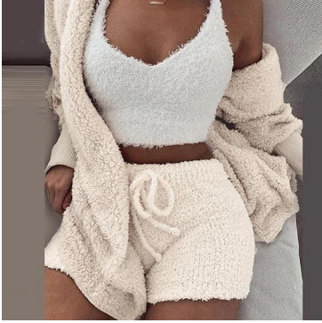 Frau in weißem, flauschigem Lounge-Set aus Strick, bestehend aus Top, Shorts und Cardigan.