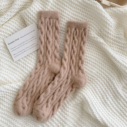 Beige Wollsocken mit Zopfmuster auf weißem Strickhintergrund, gemütliche Wintermode.