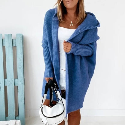 Frau in blauem Strick-Cardigan mit Kapuze, hält weiße Tasche, modisch, gemütlich.
