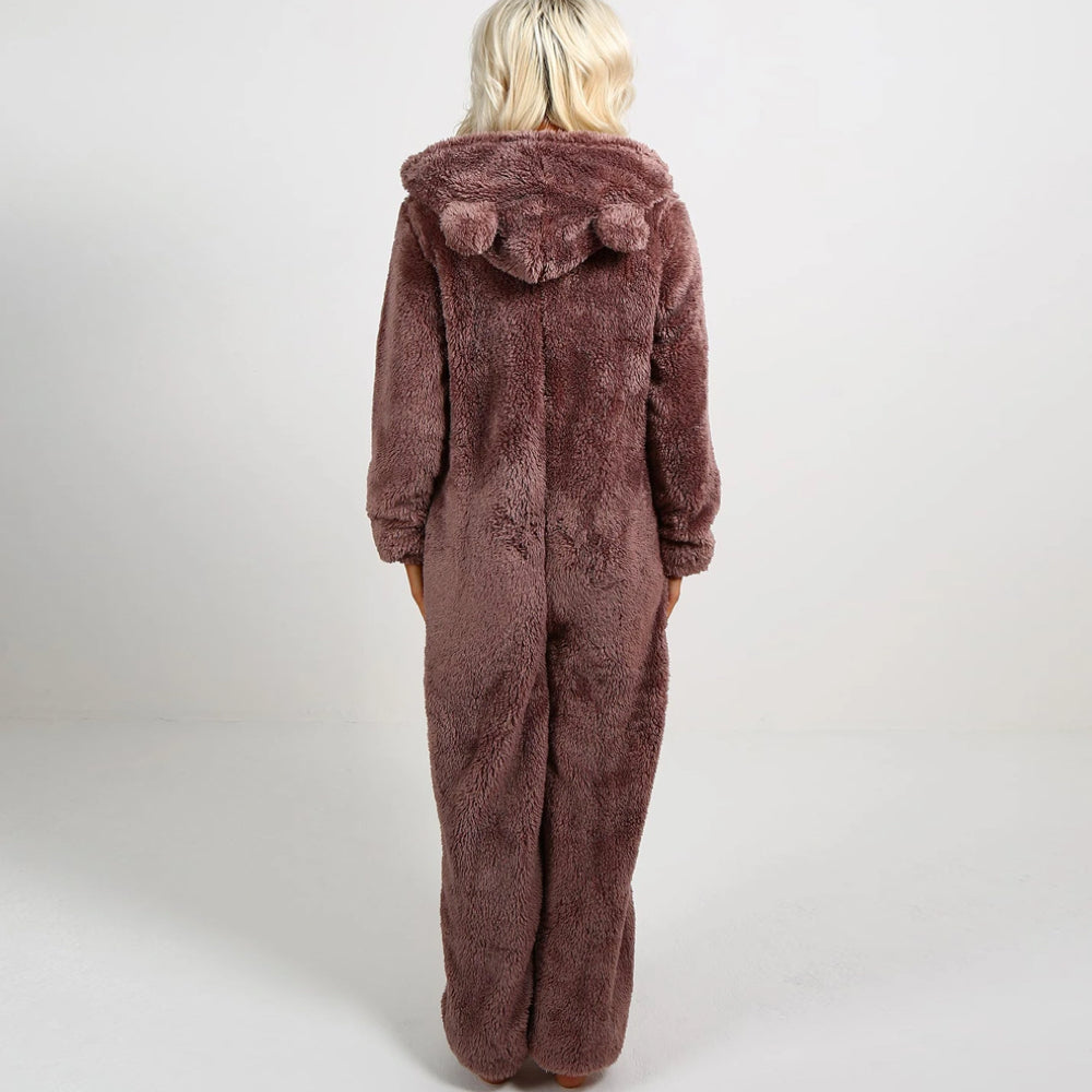 Frau in braunem Plüsch-Onesie mit Kapuze und Bommeln, gemütliche Nachtwäsche.