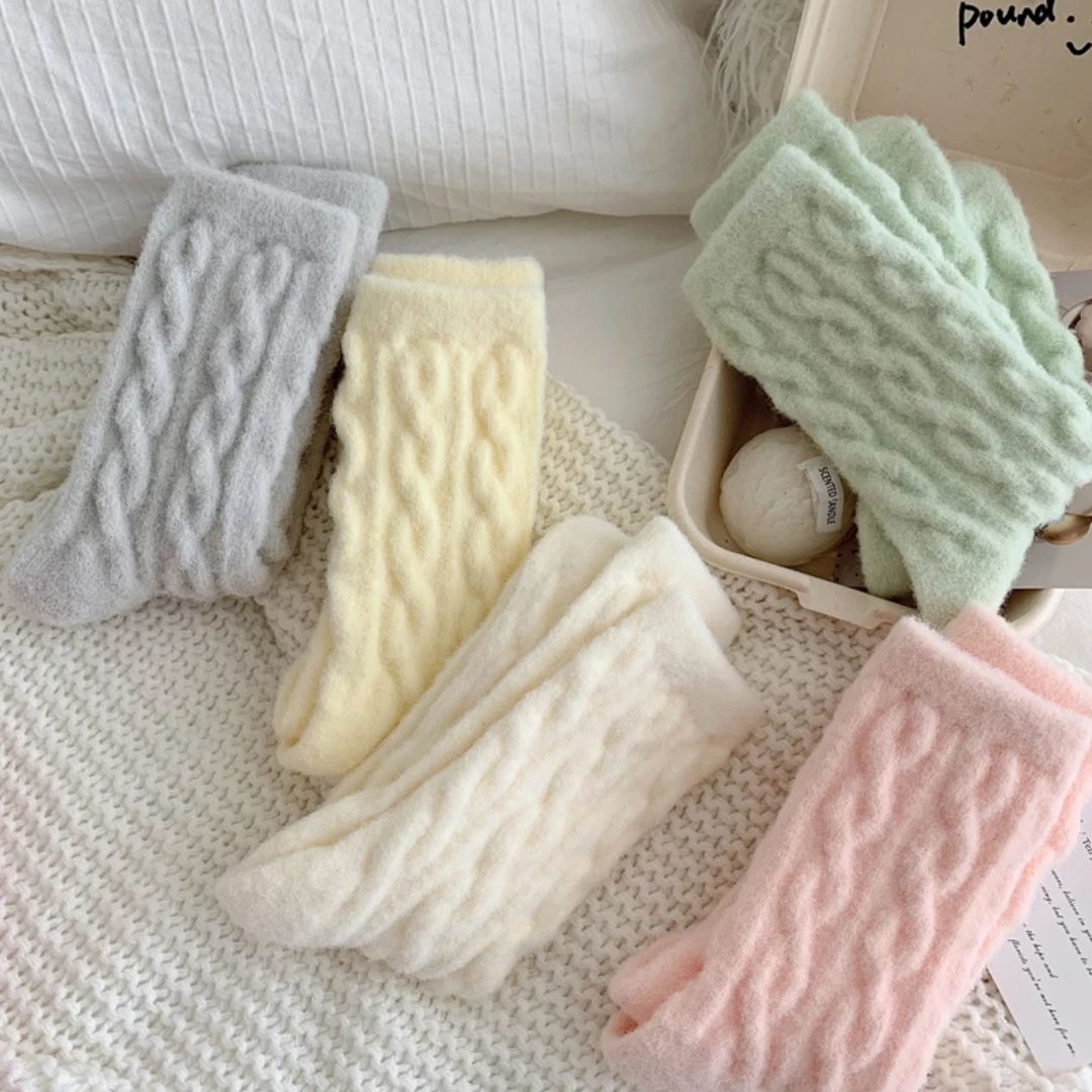Flauschige Socken in Pastellfarben, gestrickt, gemütlich, warm, für Damen, auf Bett drapiert.