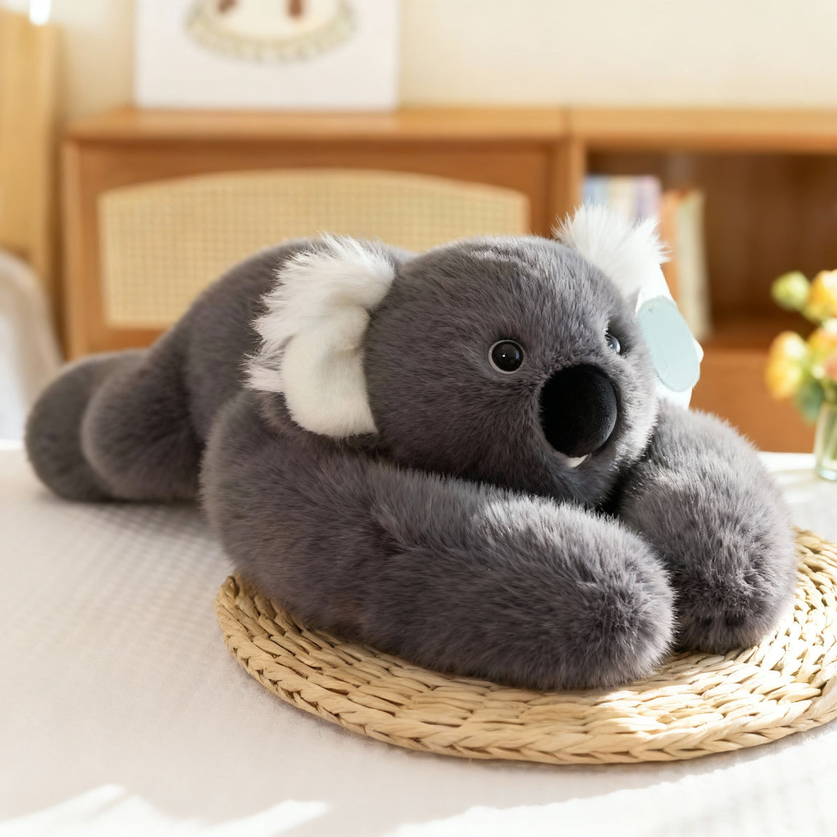 Grå koalaversion med vita lurviga öron och stor svart nos liggande på en flätad matta. 16