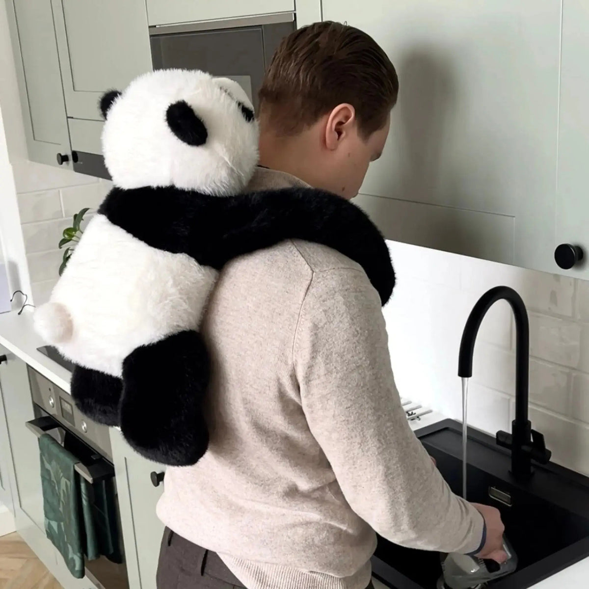 Man står vid diskbänken i köket med pandakramdjuret lindat över axlarna och hängande ner längs ryggen. 10