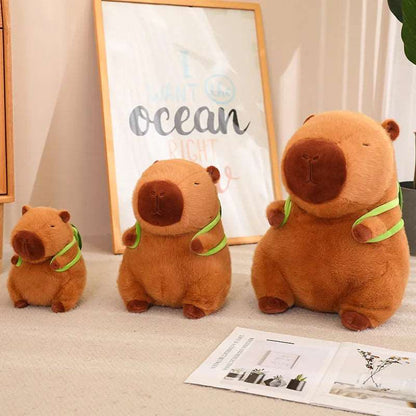 Drei braune Capybara-Plüschtiere mit grünen Schals auf Teppich, verschiedene Größen.