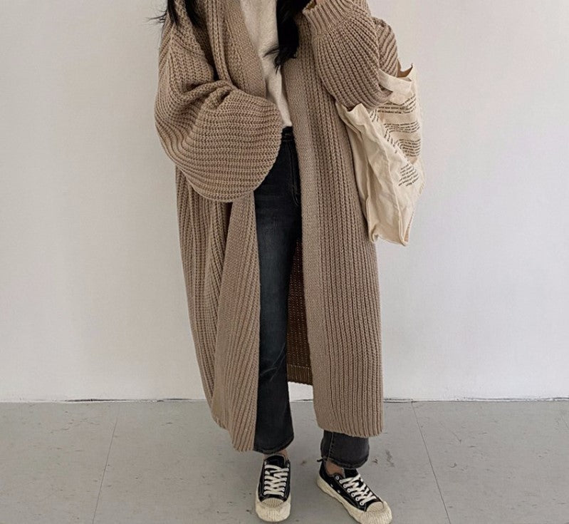Frau in langem, beige Strickmantel, schwarze Jeans, Sneakers, Stofftasche, lässiger Look.
