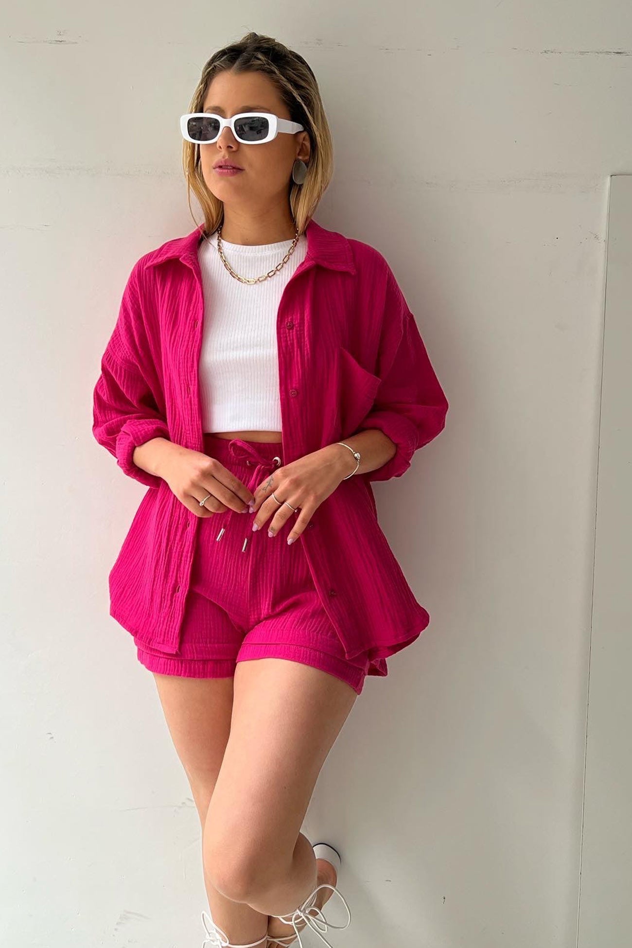 Frau in pinkem Langarmhemd und Shorts-Set, weißes Top, Sonnenbrille, modisch, lässig.