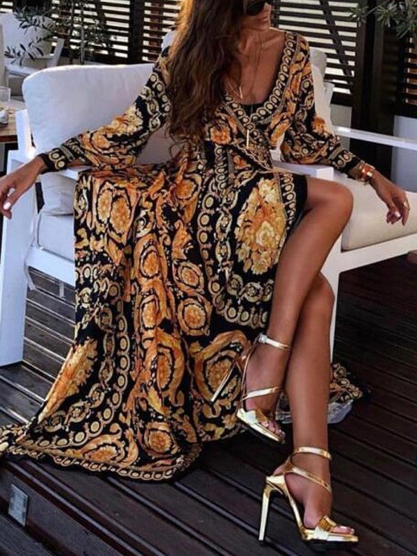 Frau in langem, gemustertem Kleid mit goldenen High Heels auf Terrasse sitzend.