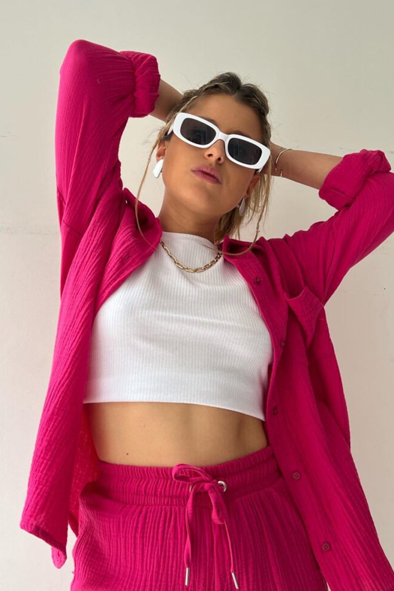 Frau in pinkem Langarmhemd und Shorts, weißes Top, Sonnenbrille, modisch, lässig.