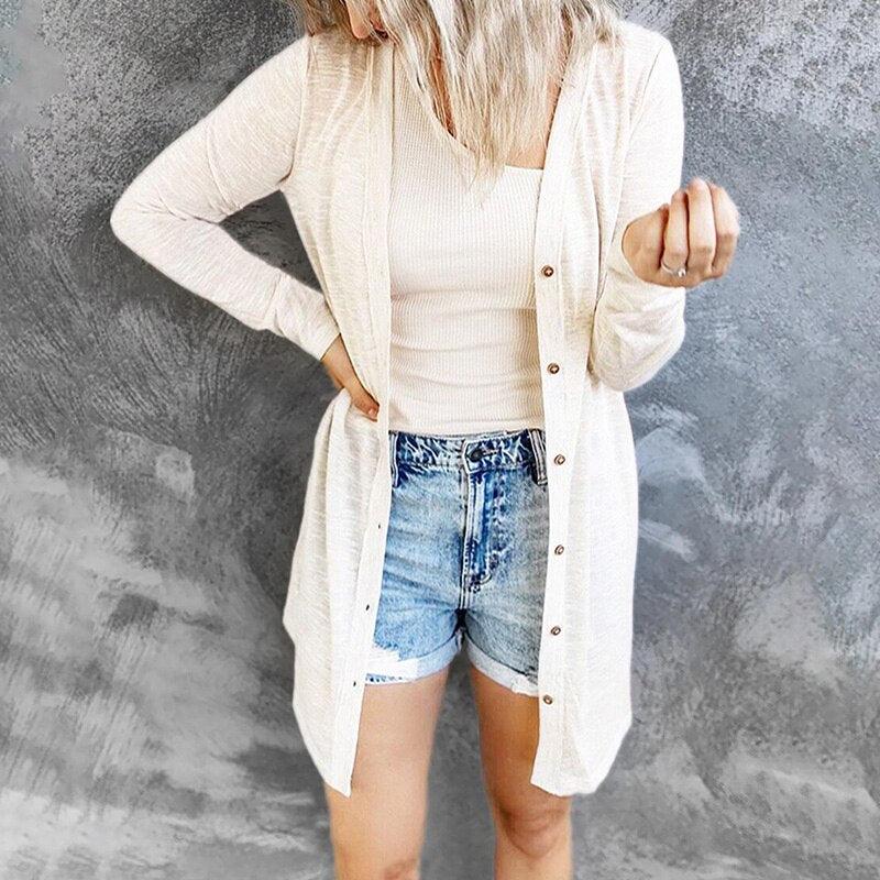 Frau in cremefarbenem Cardigan und Jeansshorts vor grauem Hintergrund.