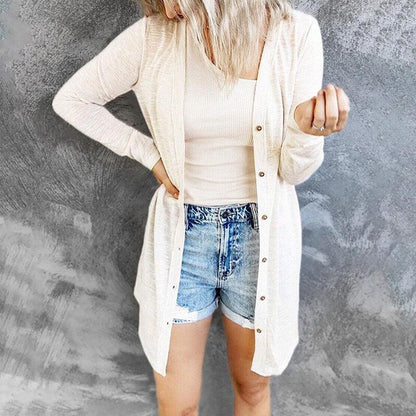 Frau in cremefarbenem Cardigan und Jeansshorts vor grauem Hintergrund.